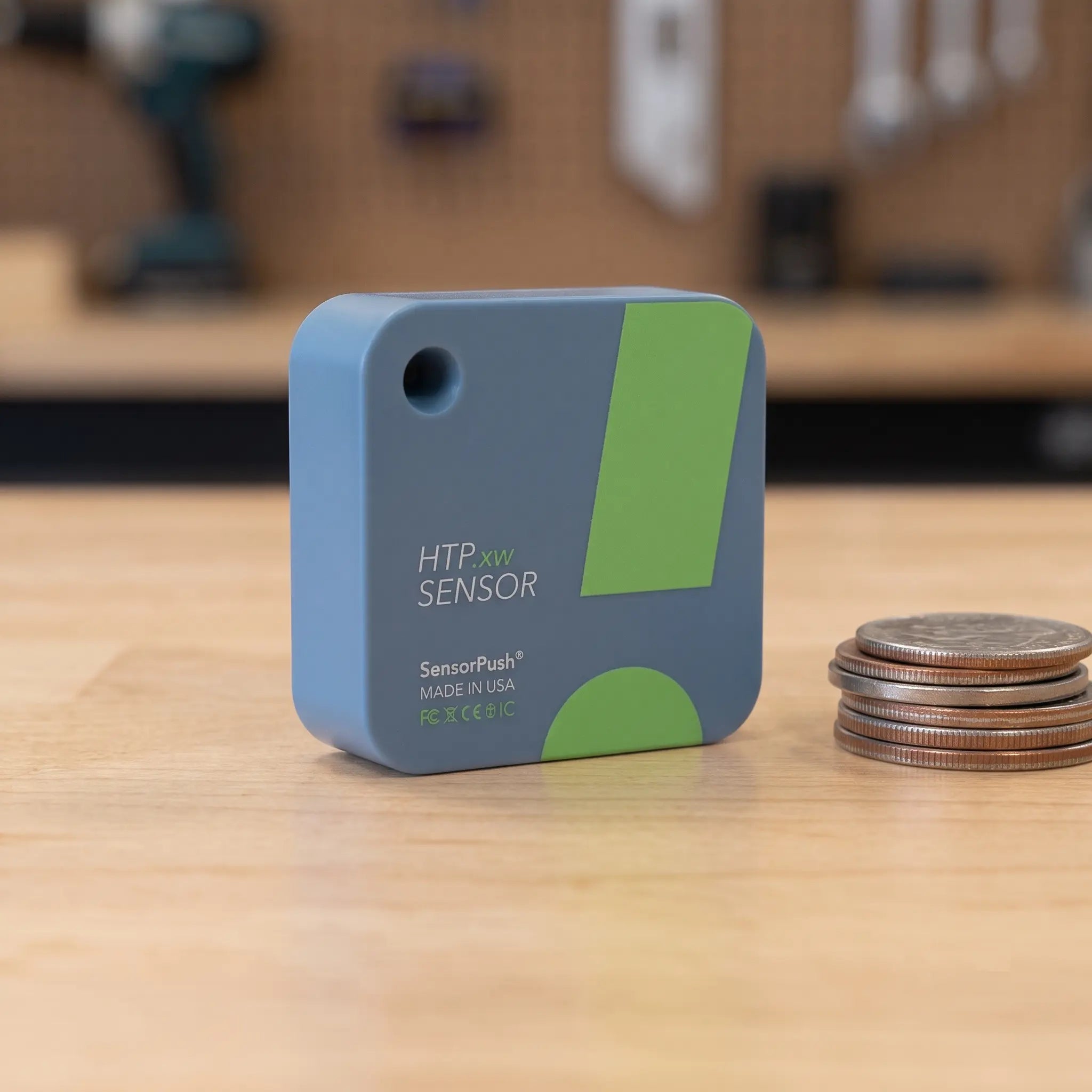SensorPush HTP.xw wireless smart environmental monitor standing next to a stack of coins for scale comparison, highlighting its compact 40x40x16.5mm size.